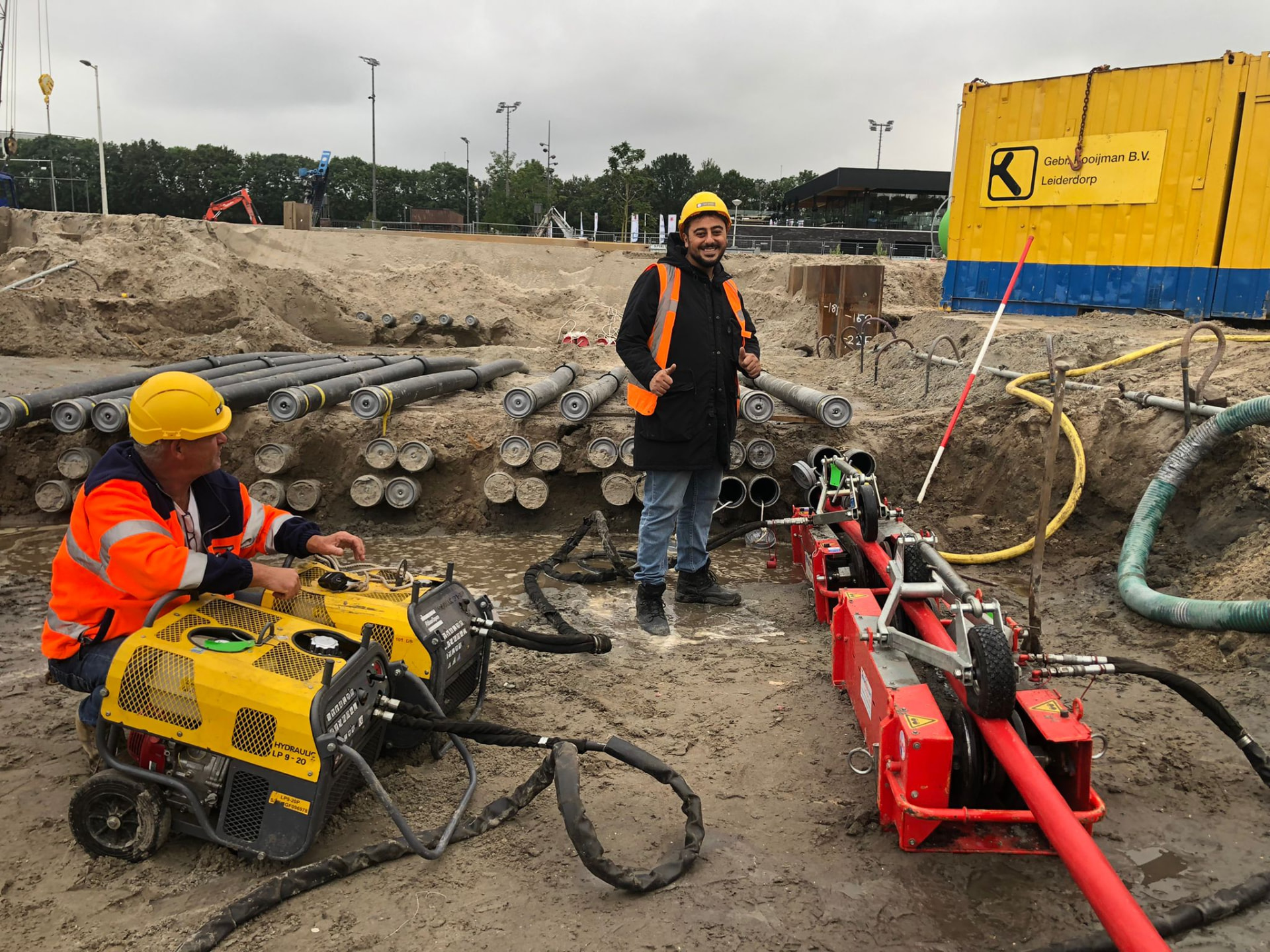 Werknemers in een sleuf met kabelmachines en buizen op een infraproject